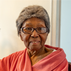 Citymeals on Wheels recipient Girlease, an older African-American woman with grey hair wearing a red bathrobe.