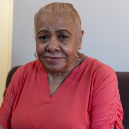 Ileana is a senior woman with brown skin wearing a peach shirt. Her white hair is up in a bun.