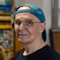 Rubem, a senior Citymeals on Wheels recipient in NYC, wears glasses and blue baseball cap.