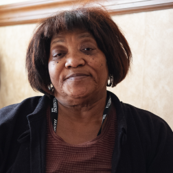 Dorothy, an older African-American woman and Citymeals on Wheels recipient in her Queens home. She has short dark hair and wears a black jacket. 