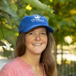 Citymeals volunteer Heather wears a blue baseball hat. She has fair skin and red hair and she is smiling. 