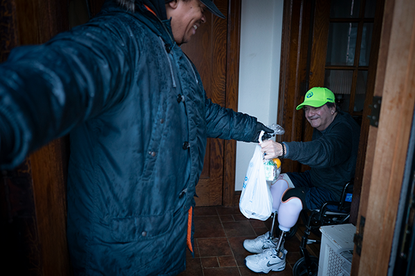 Citymeals deliverer Marco hands a meal to a senior in a wheelchair in NYC. 