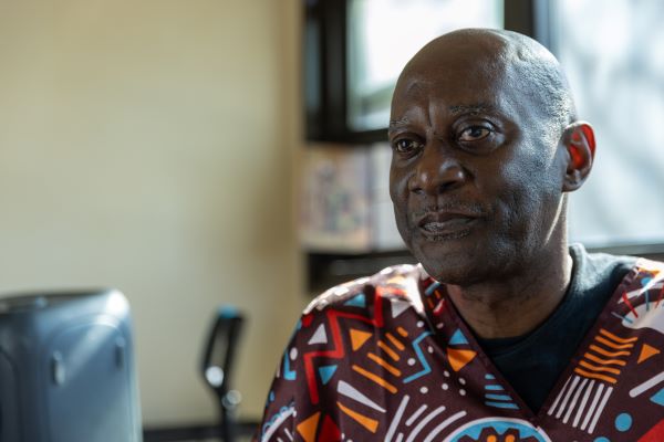 An older African American man looks at the camera. He's wearing a shirt with a colorful pattern.