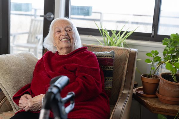 Deborah, an older woman in red, sits in an armchair. 