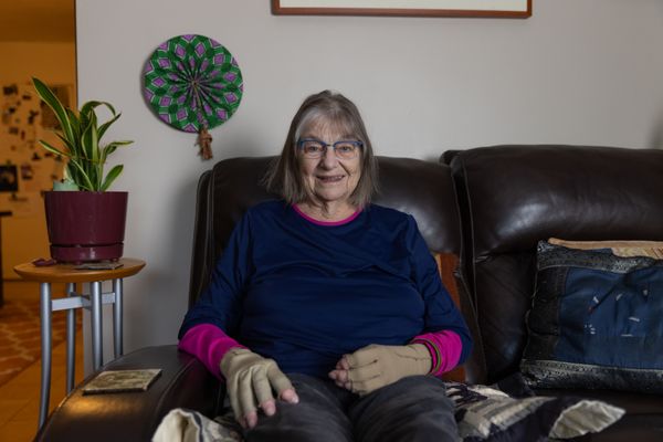 Georgia, an older woman with braces on her hands, sits on a couch, smiling.