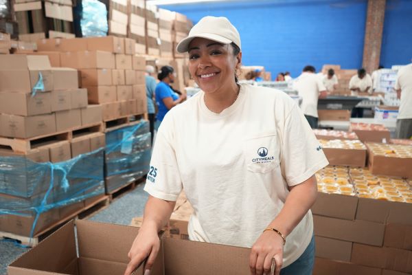 Jessica, a volunteer dressed in a white t-shirt and baseball cap, stands in front of a meal box in the distribution center. 