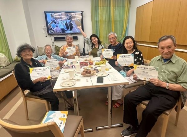 A group of older adults, holding up certificates, showing that they have participated in Life Story Club.