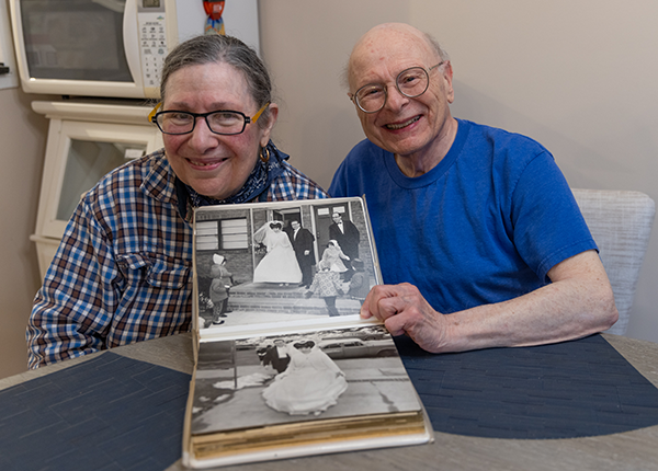 Citymeals on Wheels recipients Caryn and Michael show off their wedding photo album in their NYC apartment. 