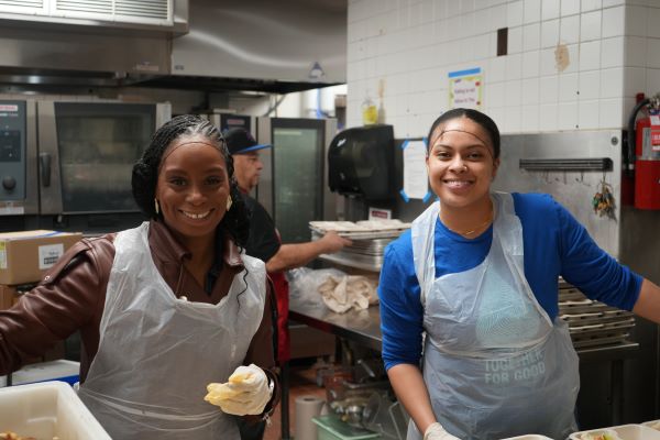 Two female volunteers wearing hairnets, smiling as they stand in a meal center kitchen. 