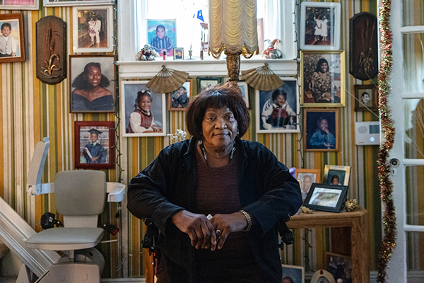 Dorothy, Citymeals recipient, in her NYC apartment, surrounded by family photos. A wheelchair lift is by her staircase. She relies on meals on wheels for food. 