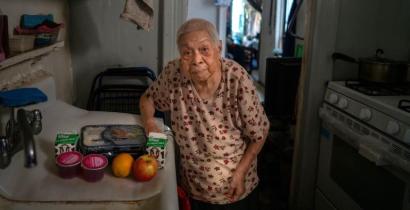 An older Asian American woman standing in her kitchen, a home-delivered meal next to her on the counter.