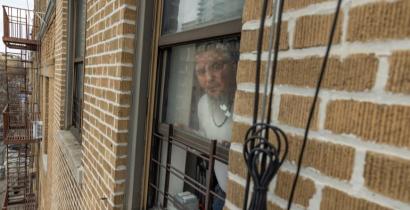 An older man looking out an apartment window. 