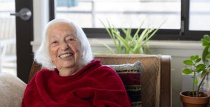 An older woman with white hair smiling, wearing a red shirt. 